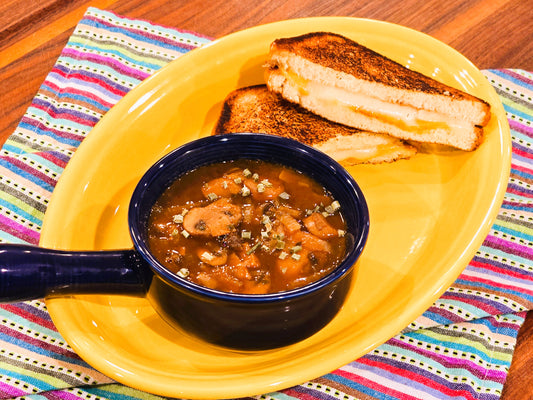 Image of a mushroom and onion soup with a grilled cheese sandwich on the side.